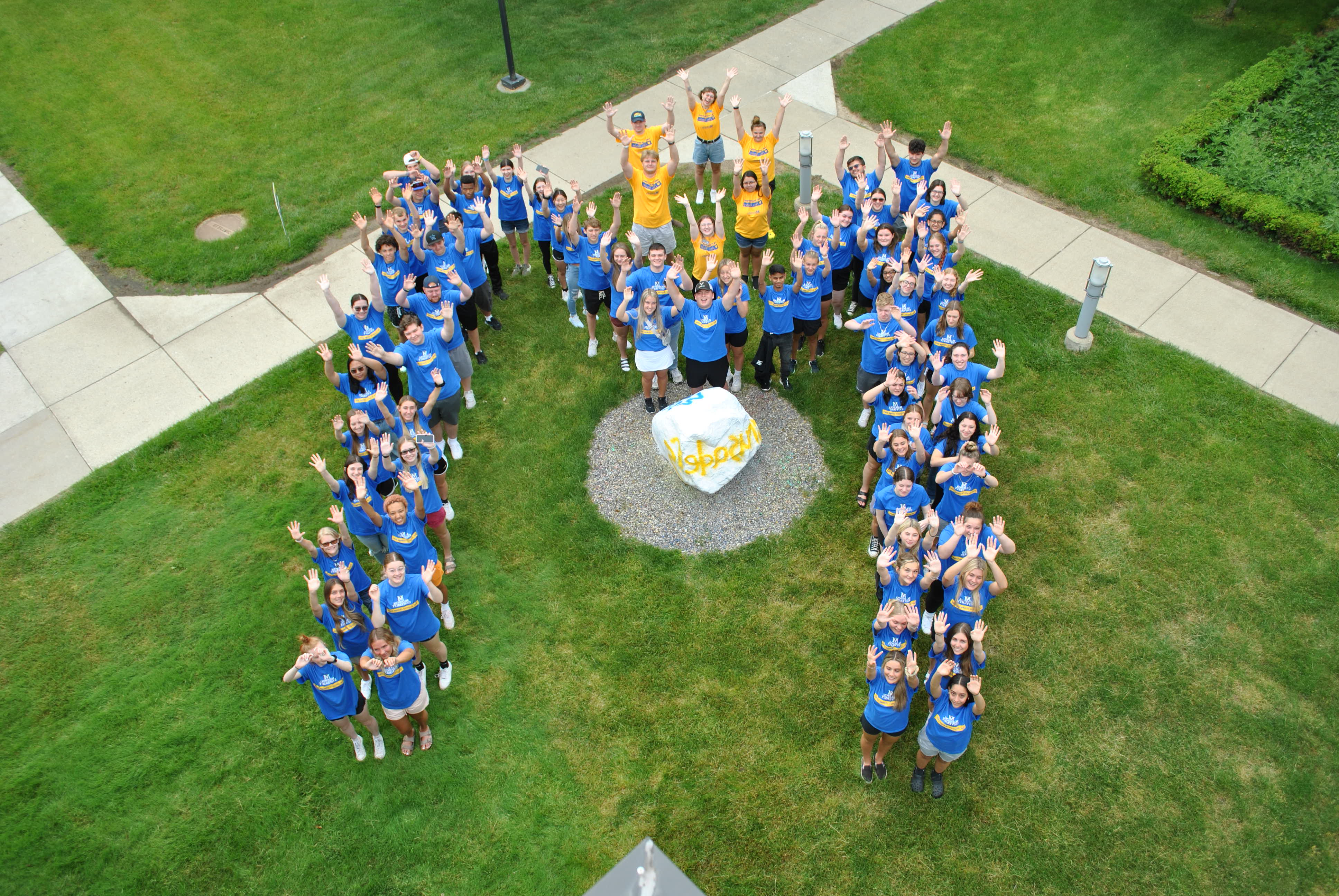 Orientation prospective students and peer mentor making the shape of the Madonna M around the school rock